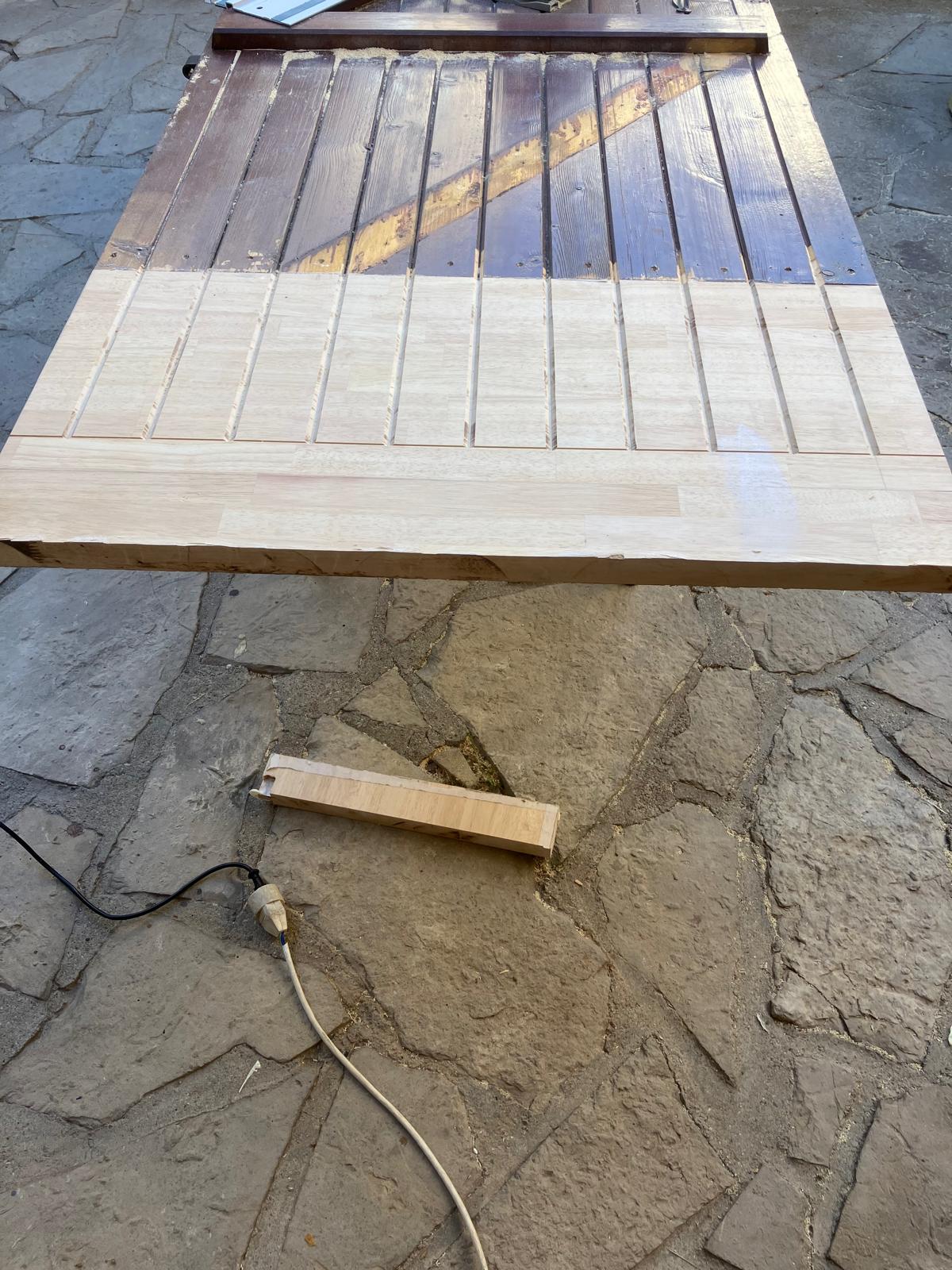 Porte en bois partiellement poncée sur sol en pierre.